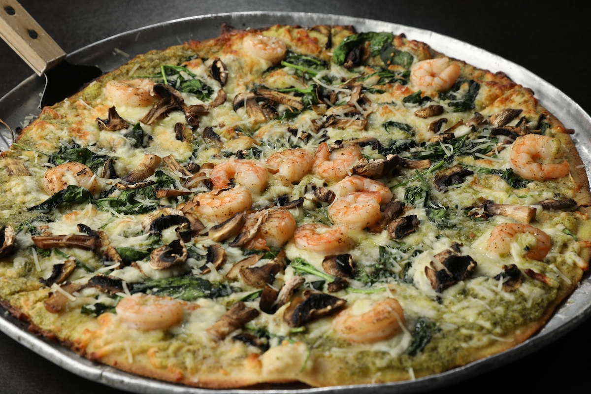 A pizza with mushrooms, green sauce and shrimp, with cheese grated on top.