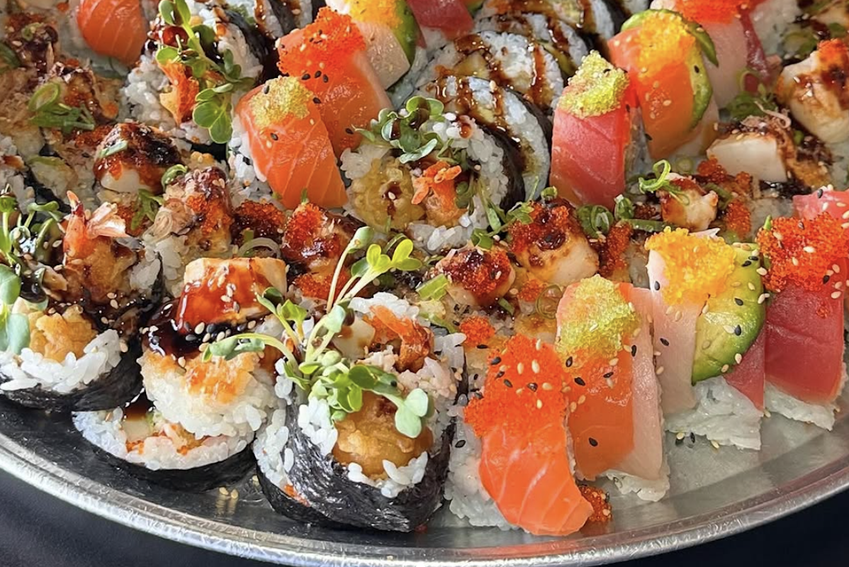 Sushi lined up on a tray, including sushi wrapped in seaweed and sushi with roe or fish on top.