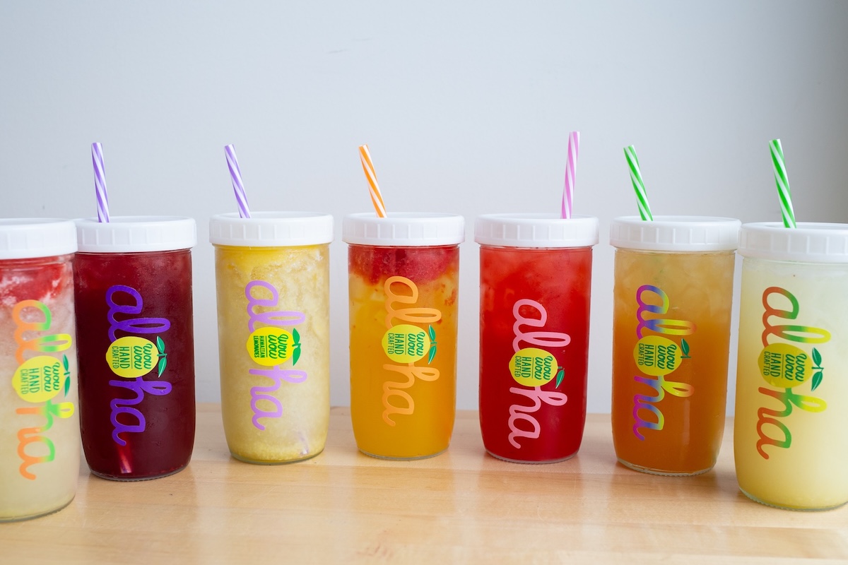 A line of seven cups of colorful drinks with straws.