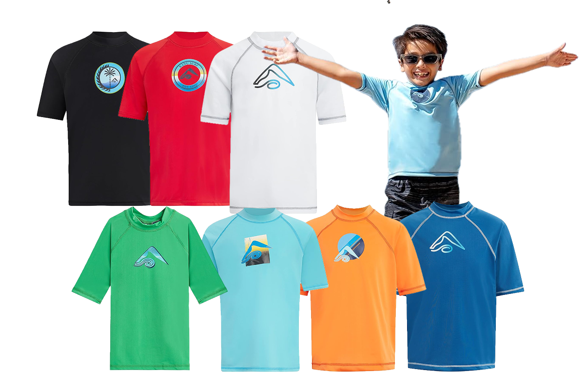 A young boy, wearing sunglasses, a blue shirt, black shorts, has his arms stretched out in front of him. He is surrounded by short sleeved shirts in the colors black, red, white, green, light blue, orange, and blue.