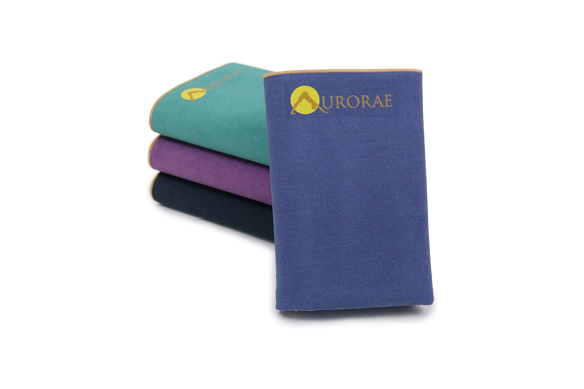 This image features four folded yoga mats: three stacked—black, purple, and teal blue—next to an upright folded blue mat.