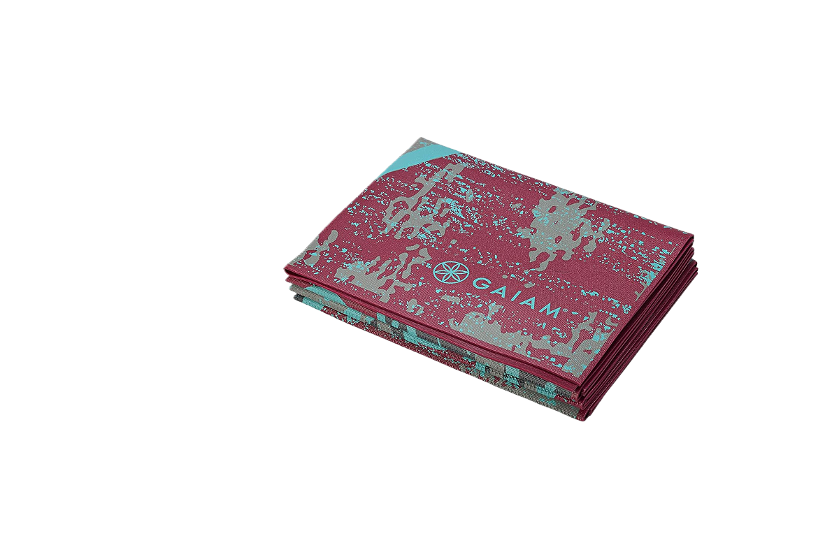 This image features a folded Gaiam travel yoga mat featuring a red and turquoise artistic design with a stylized leafy pattern. The brand name "GAIAM" and logo are visible on the mat.