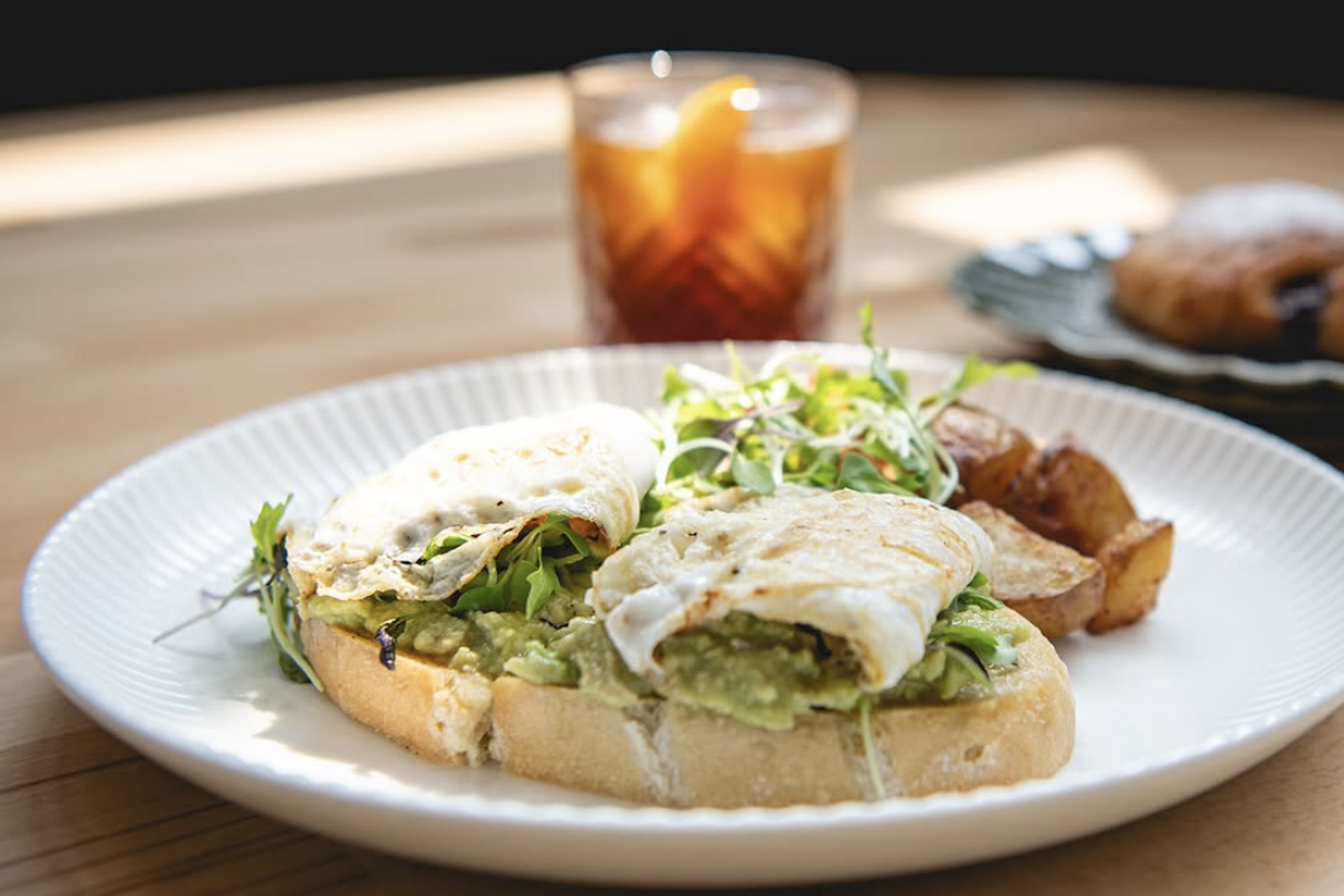 An omelet on avocado toast topped with microgreens and a side of potatoes.