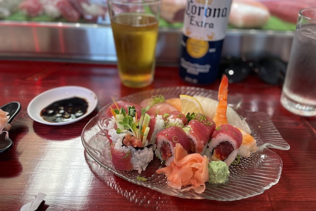 A plate of sushi garnished with microgreens, prawns, lemon slices, ginger, wasabi and green onions.