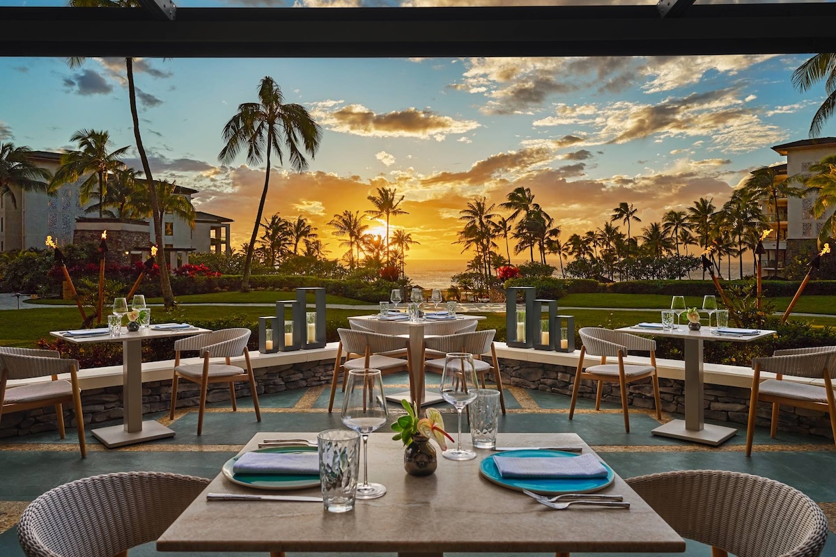 Restaurant seating on an outdoor patio with a sunset in the background.
