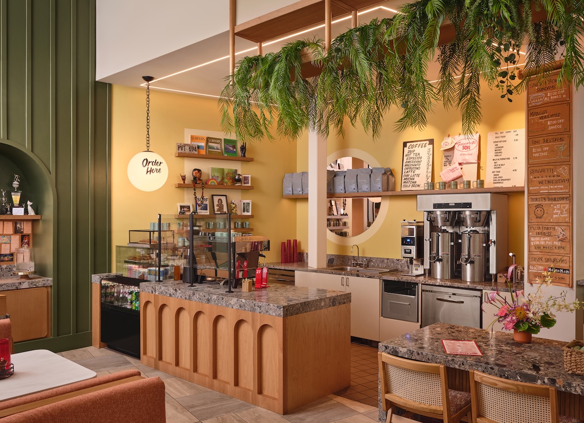 A restaurant with yellow walls, greenery, warm woods and an inviting ambience.