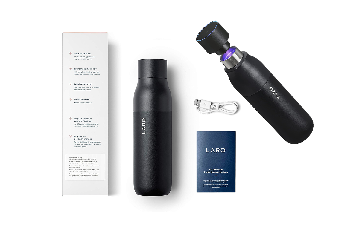 A white box with written instructions on it next to a black metal water bottle, next to a charging cord and pack of wipes underneath a black metal water bottle, with the cap unscrewed with a faint blue light in it.