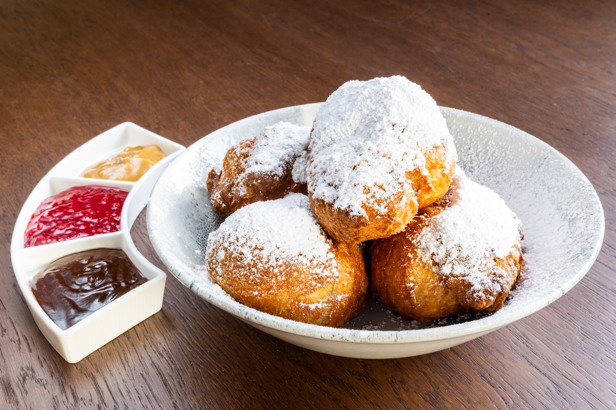 A plate with puffed pastries coated with powdered sugar and three different sauces on the side.