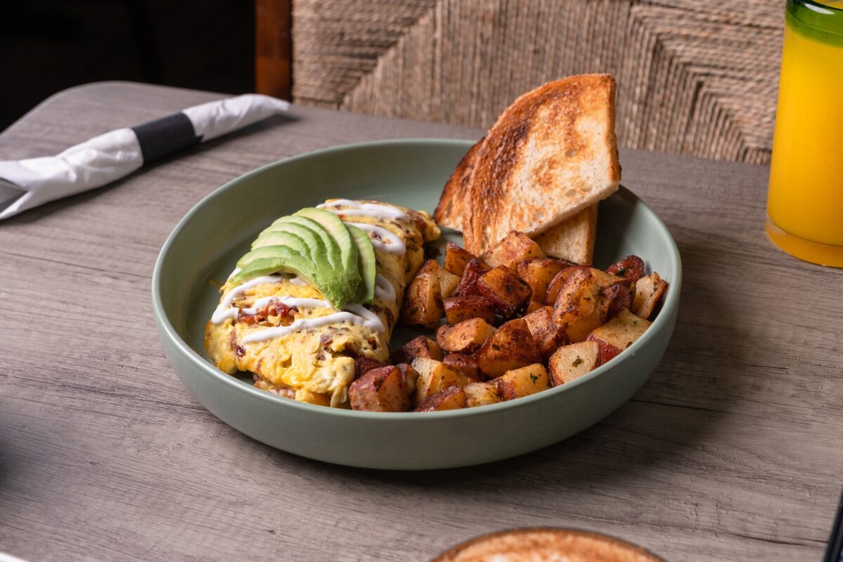 A bowl with breakfast potatoes, eggs, avocado and a crisped bread.