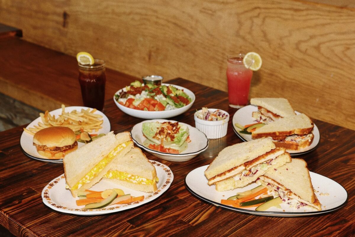 A tablescape with plates of food including sandwiches and salad.