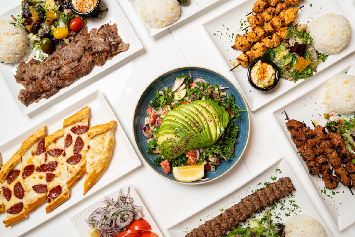An aerial shot of a tablescape with plates including flatbread, avocado salad and meat.