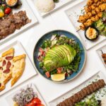 An aerial shot of a tablescape with plates including flatbread, avocado salad and meat.