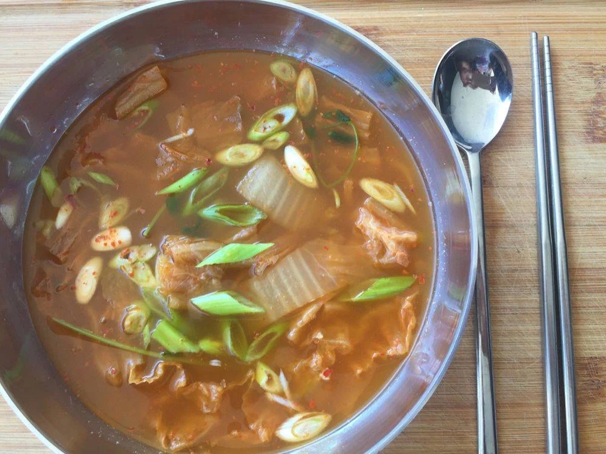 Bird's eye view of a bowl of soup with some veggies, and a spoon next to it.