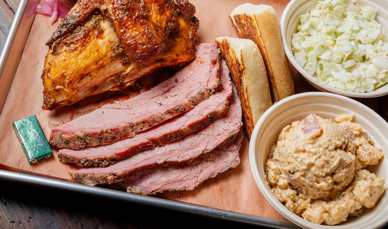 A tray lined with paper and slices of barbecued meat and sides.