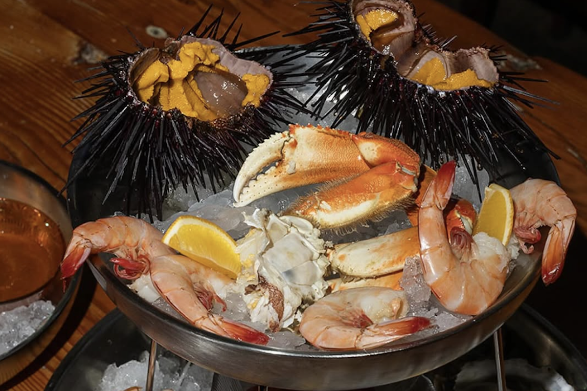 In a bowl with a bed of ice sit crab legs, prawns and sea urchin.