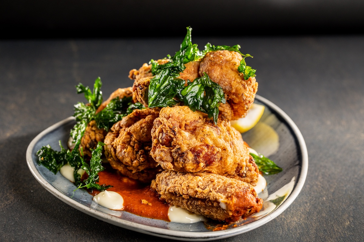 A plate with breaded and fried chicken, topped with greens and dollops of red and white sauce.