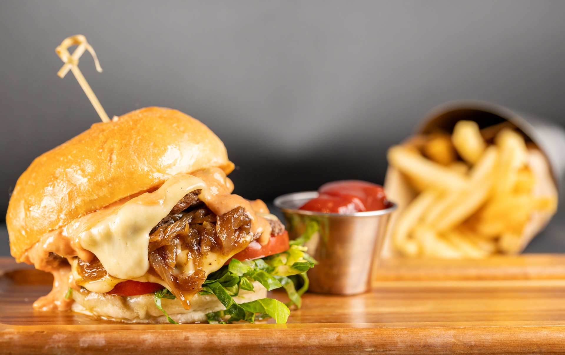 A burger with lots of sauce, lettuce and grilled onions and some ketchup and fries in the background.