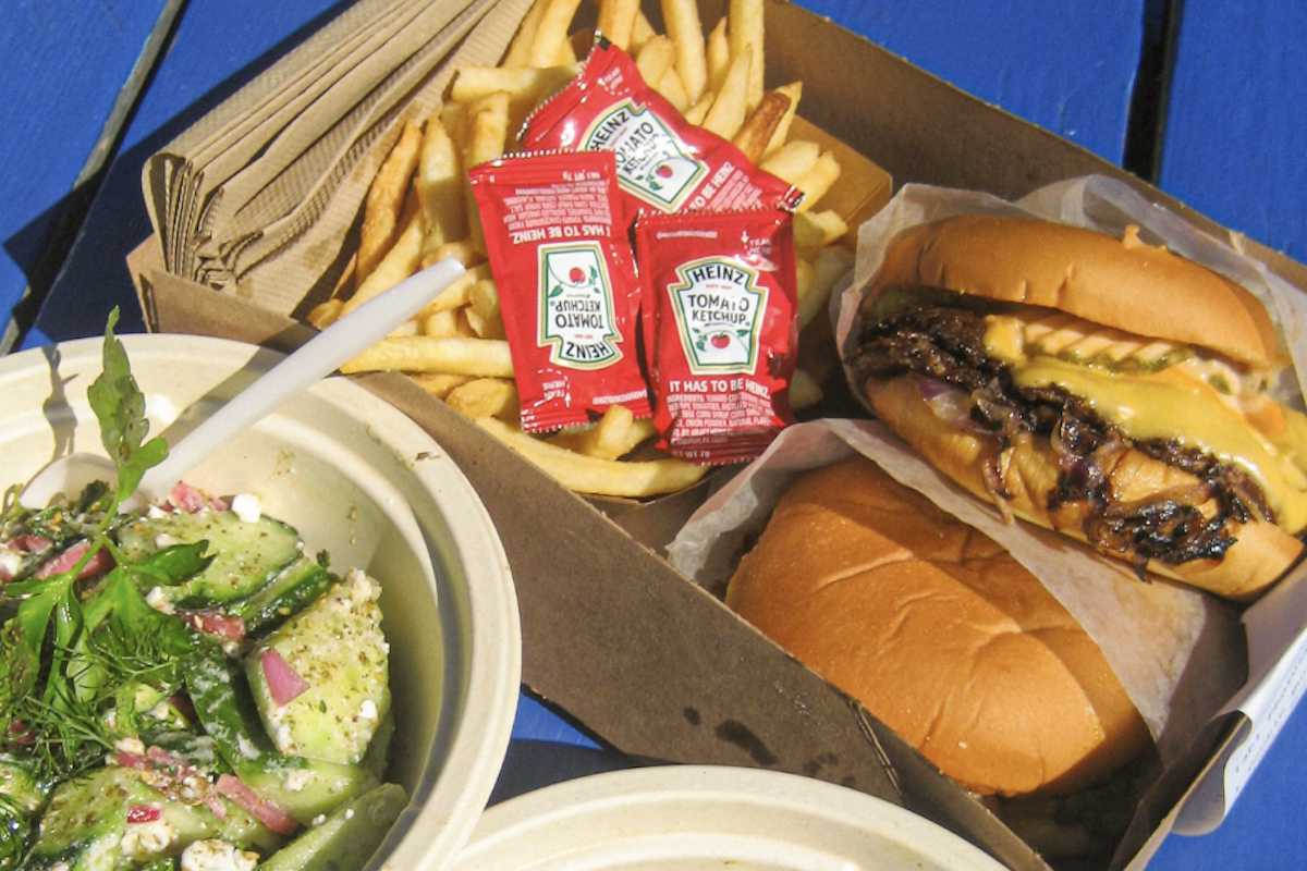 An aerial shot with a container that has a burger, fries, packets of ketchup and a salad.