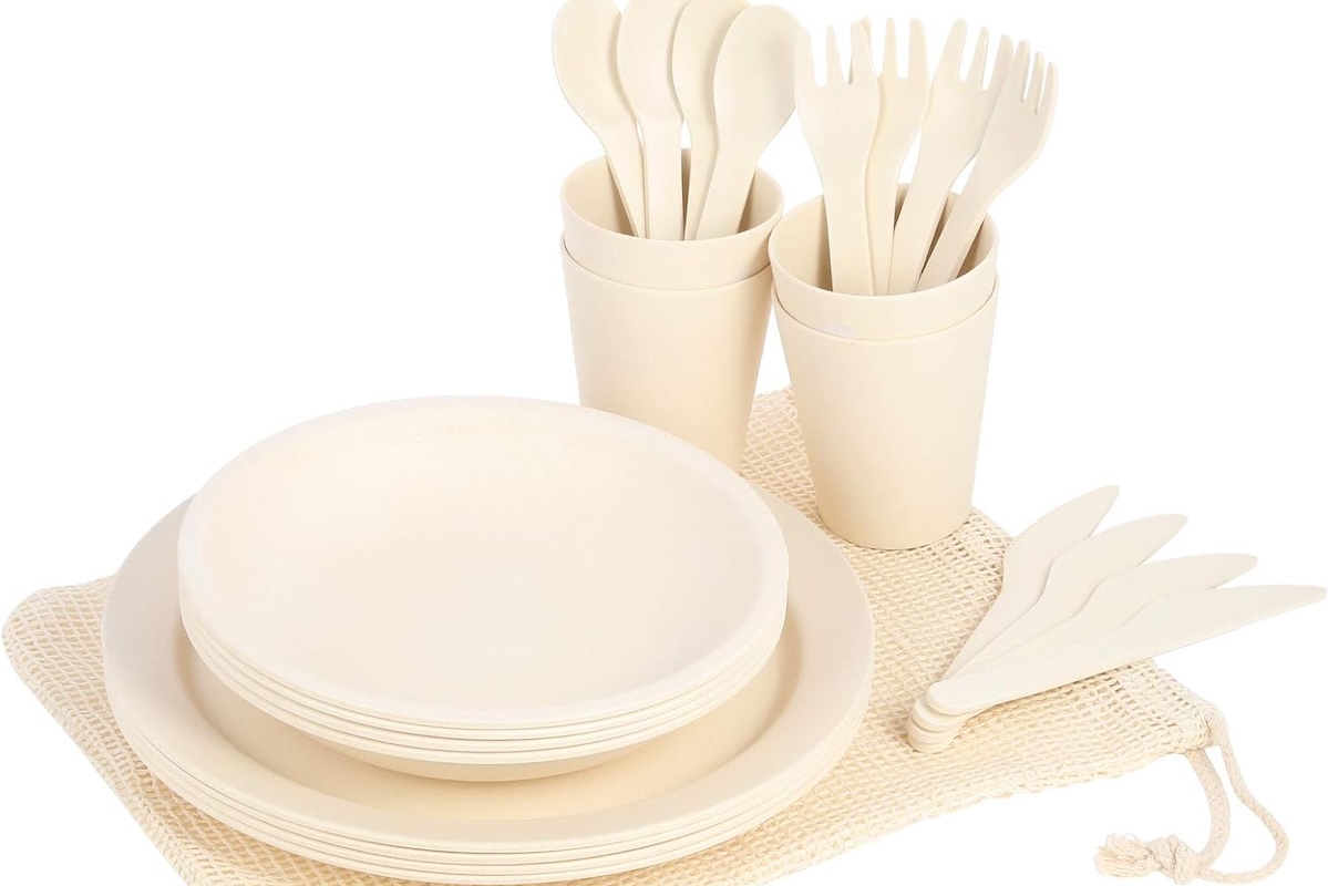 A set of offwhite bamboo dinnerware, including plates, bowls, cups, spoons, forks, knives and a mesh travel bag.