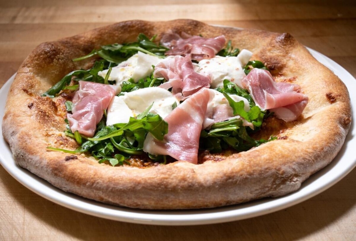 A thick crust pizza with arugula, ham and burrata.