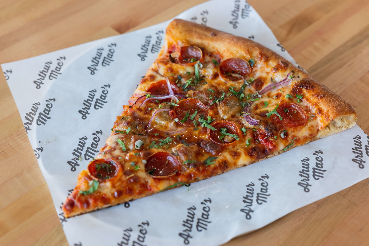 One slice of pizza on a piece of paper with cheese, pepperoni and chopped herbs.