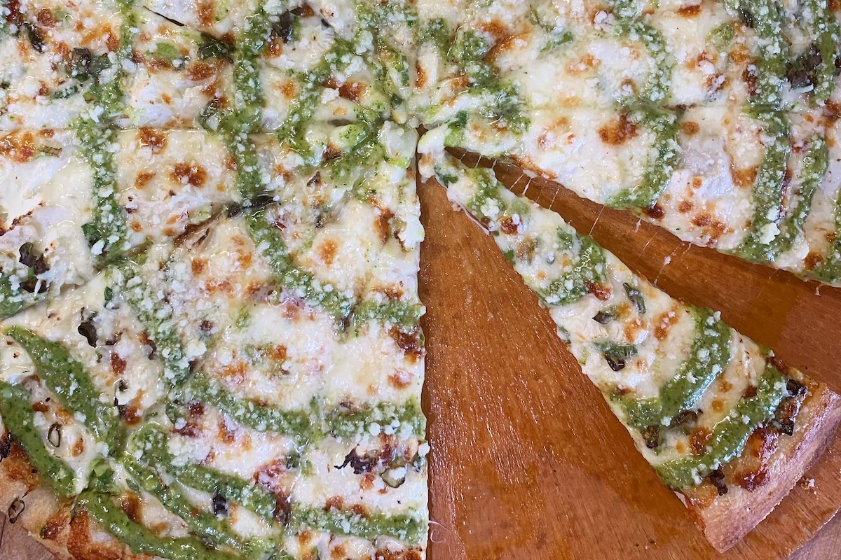 A pizza with white sauce for the base and a swirl of pesto sprinkled with parmesan, with a few slices removed.