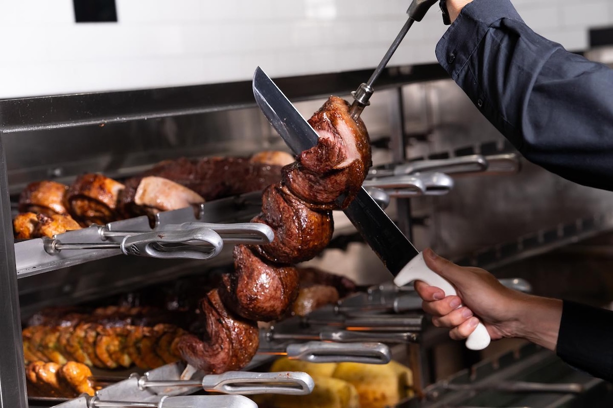 A chef slices a sirloin steak on a skewer off of a rotating grill.
