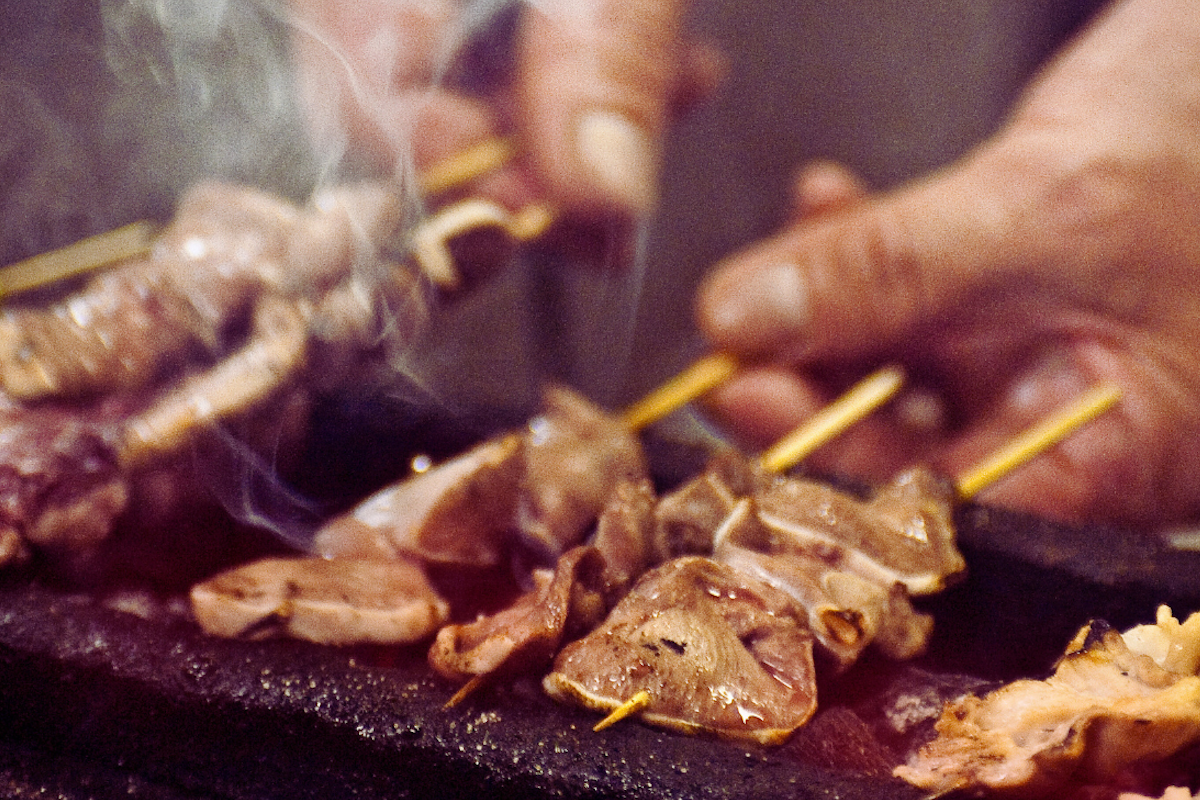 Person grilling skewered meat on a grill.