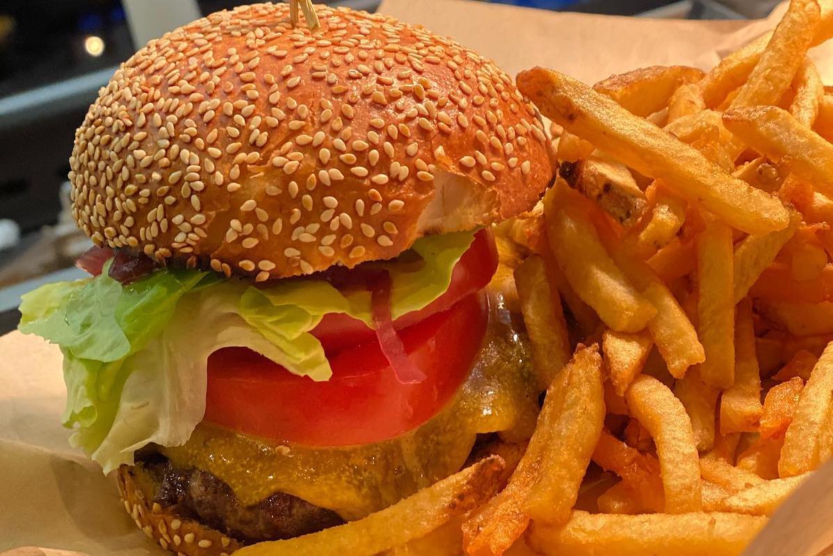 A burger with a sesame seed bun, lettuce, cheese and tomato, with fries on the side.