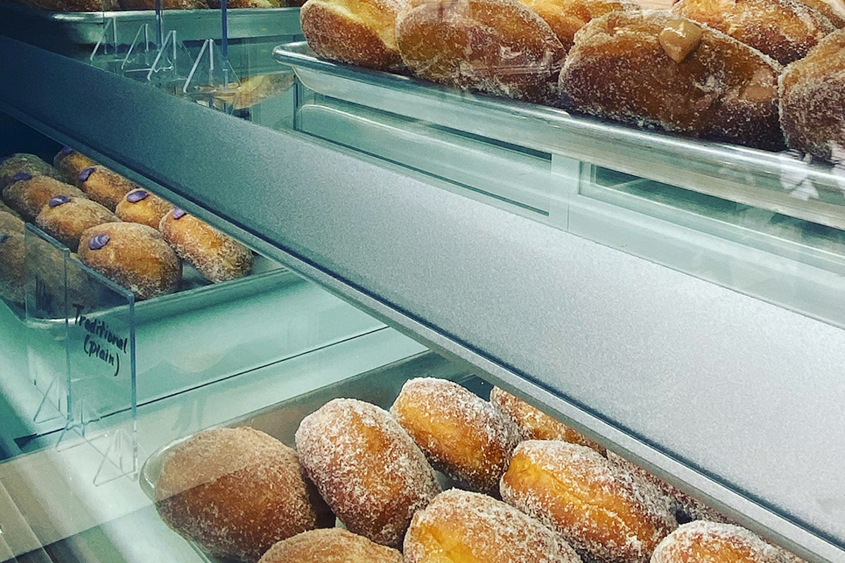 Sugared donuts sit behind a glass case.