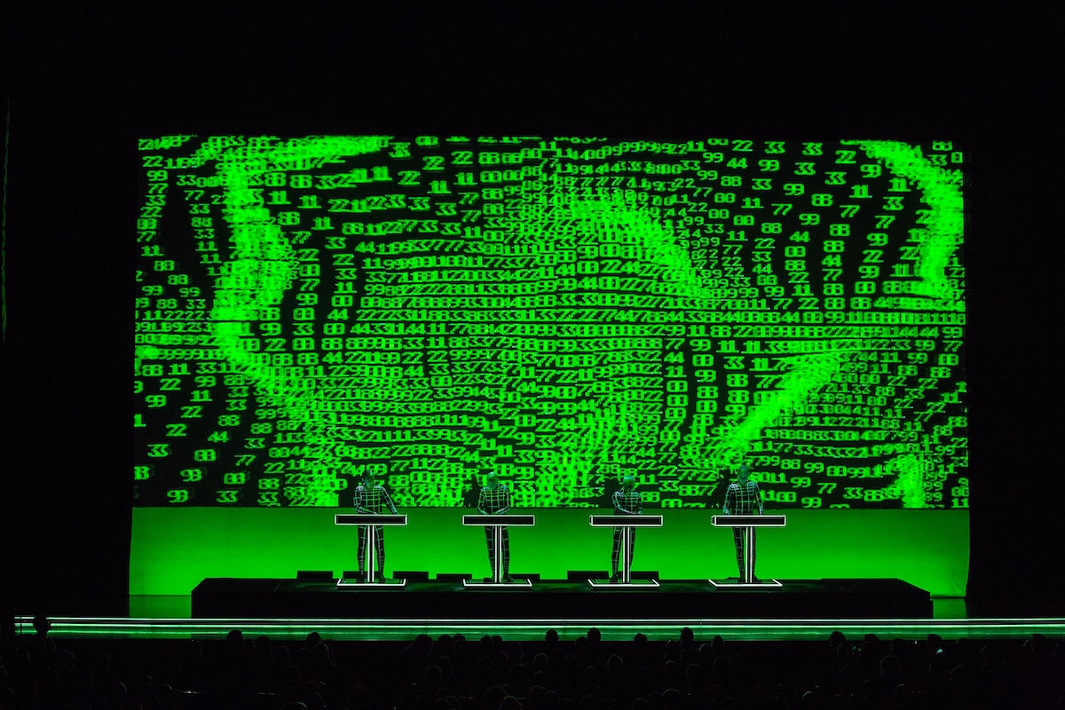 Four DJs in front of a green and black art display that looks like computer processing