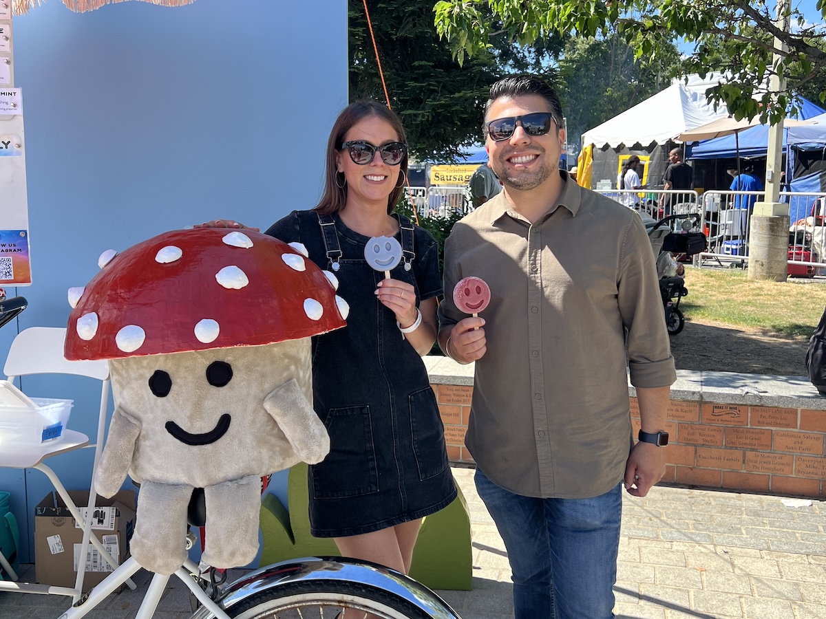 Two people pose with a large mushroom plushie