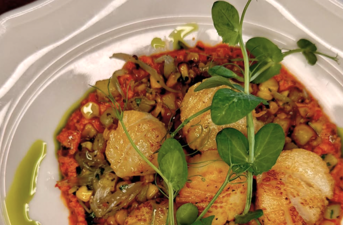 A reddish dip and some scallops sit on a plate.