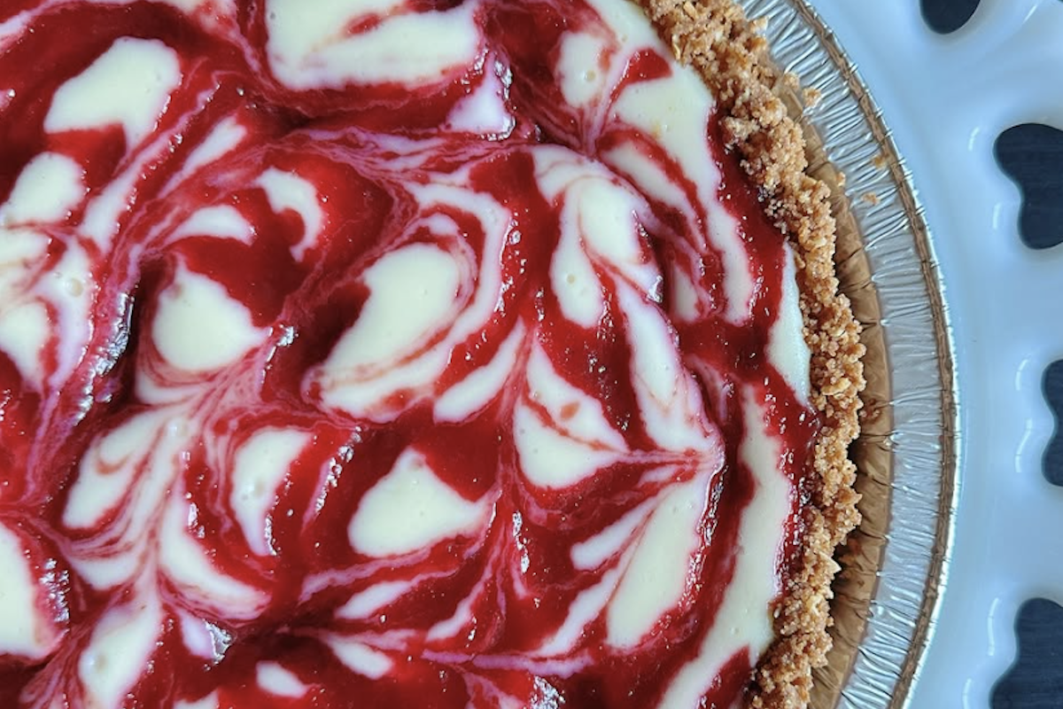 A close up shot of a red and white marbled cheesecake on a white glass platter.