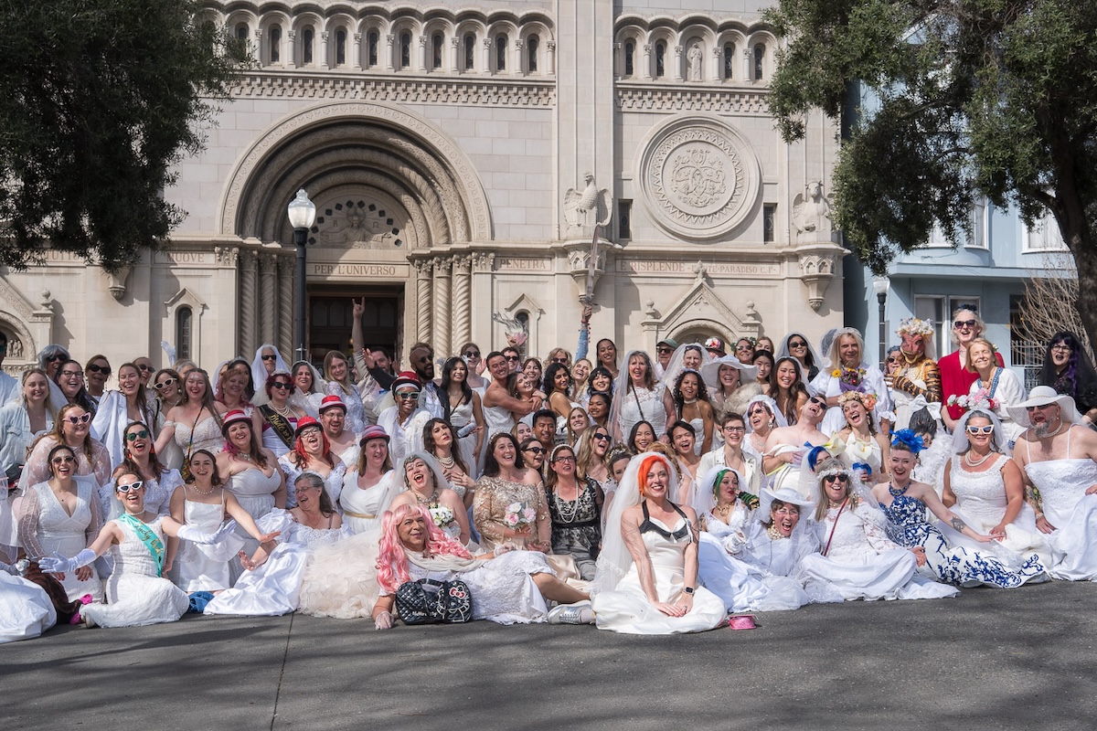 A large group of people in wedding dresses pose in front of a church in San Francisco's North Beach neighborhood