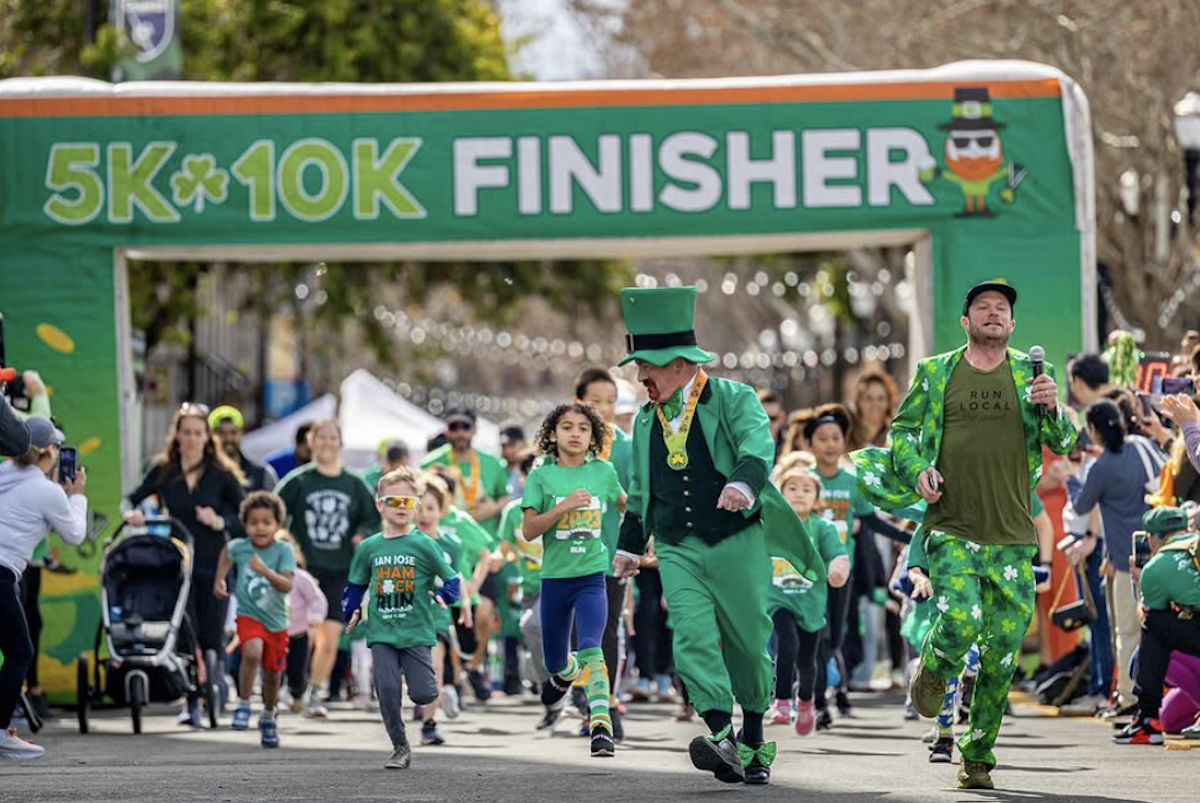 A man running dressed as a leprechaun is followed by kids dressed in lots of green through with a sign for a 5K and 10K finish line in the background.