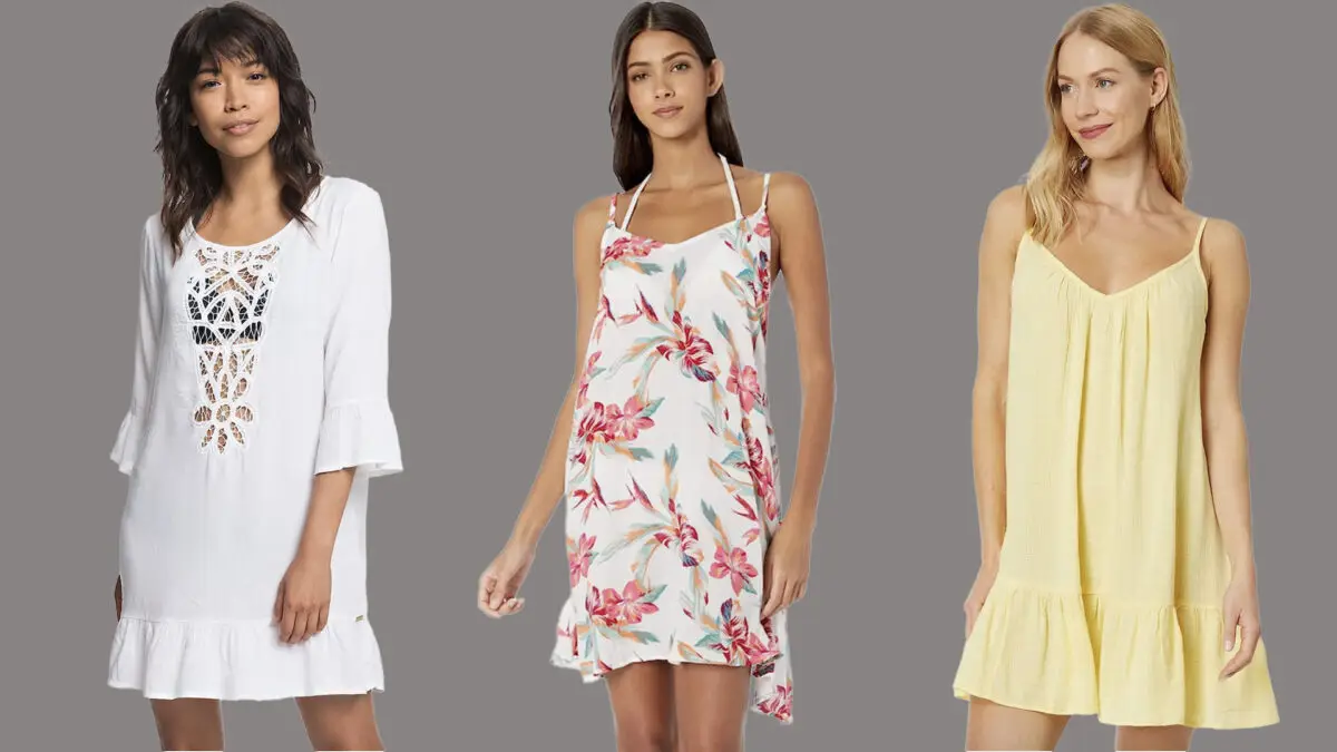 Three women stand against a gray background, each wearing a different dress. The left wears a white dress with crochet detailing and ruffled sleeves, the middle dons a white dress with a pink floral pattern and spaghetti straps, while the right is in a yellow sleeveless dress—perfect climate-friendly beach cover-ups.