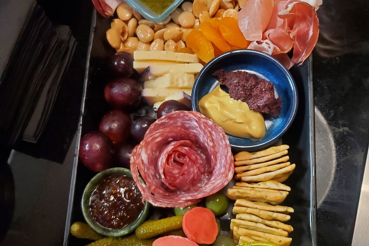 A charcuterie tray with a salami rose, olives, crackers, veggies, nuts, cheeses and more.