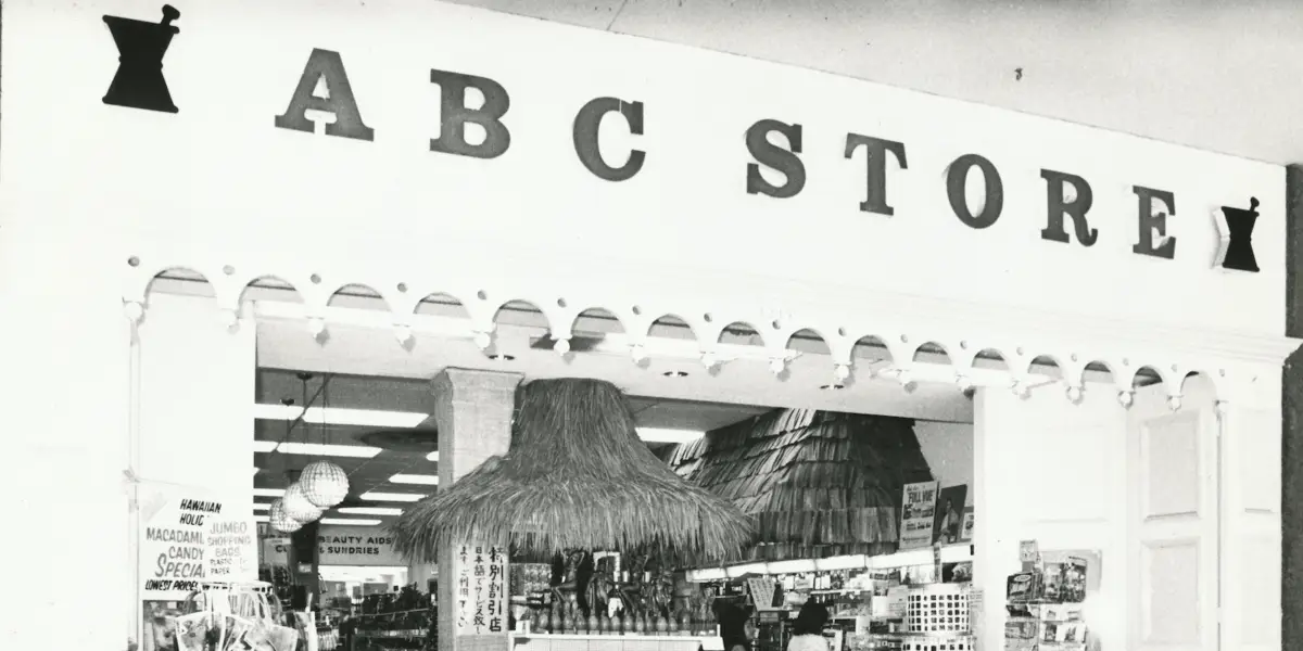 A black-and-white image of the entrance to a family-owned ABC Store. The sign reads "ABC STORE" in large letters. Inside, the store is filled with various items, and a thatched-roof display is visible in the center. The storefront has decorative elements around the entrance.