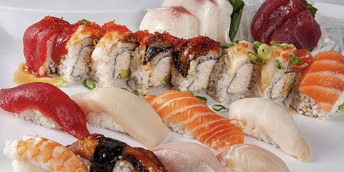 A platter of the best sushi in South Bay is displayed on a white plate, featuring assorted sushi and sashimi. The arrangement includes various sushi rolls topped with fish and roe, alongside nigiri with tuna, salmon, and shrimp atop rice.