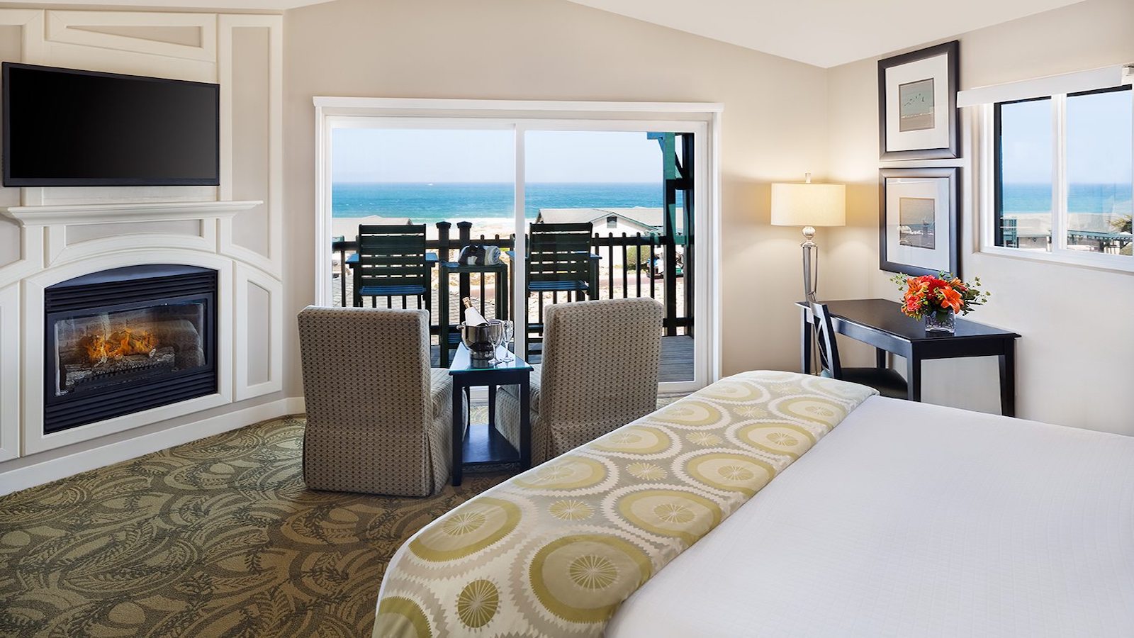 Queen bed, fireplace and a balcony connected to a hotel room at Sanctuary Beach Resort in Monterey, California.