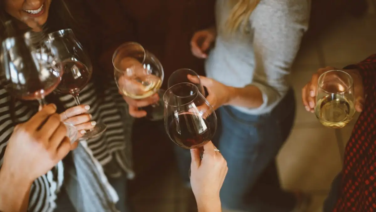 A group of people stand closely together, each holding a glass of wine. The scene captures their hands and glasses as they toast during a holiday meal. The image features a variety of wine colors, including red, white, and rosé, perfect wine pairings with their festive dishes. Some individuals wear casual clothing.