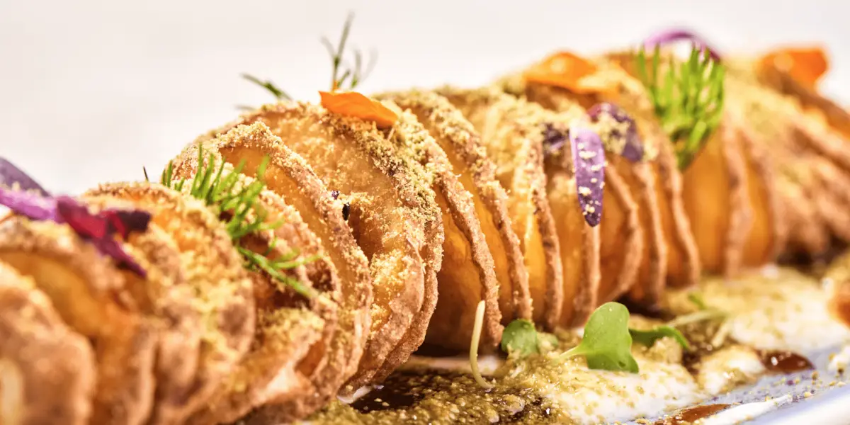 Crispy spiral potatoes garnished with colorful herbs and flowers, served on a bed of creamy sauce and sprinkled with breadcrumbs. This delightful potato dish is presented in a visually appealing manner, highlighting their golden-brown texture.