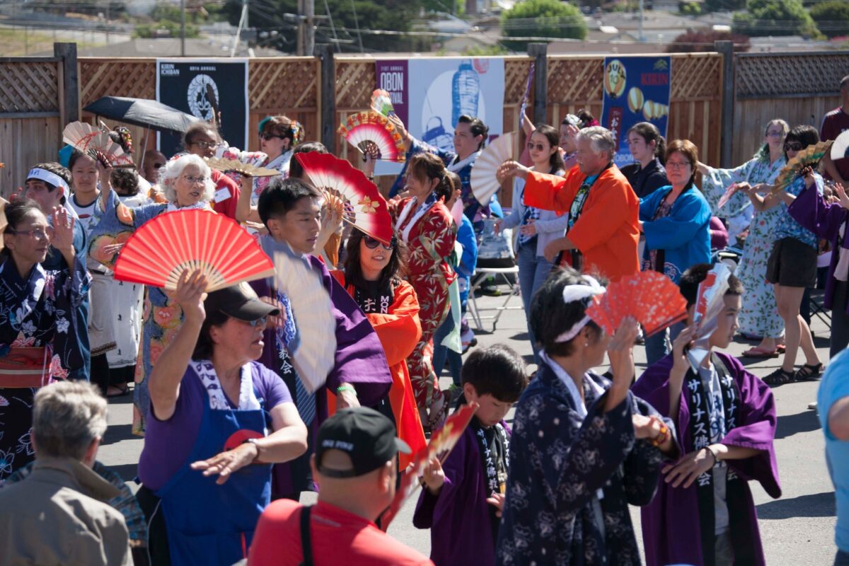 Festivalgoers in traditional Japanese dress hold fans and walk in circle at Obon Festival on the Monterey Peninsula, in California