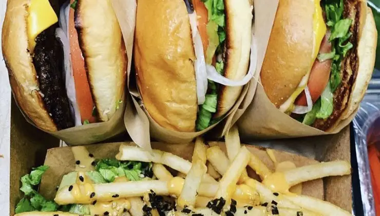 Three of the best burgers on the Big Island, wrapped with lettuce, tomato, and onions, are lined up side by side above a serving of seasoned french fries topped with sauce, shredded lettuce, and sesame seeds.