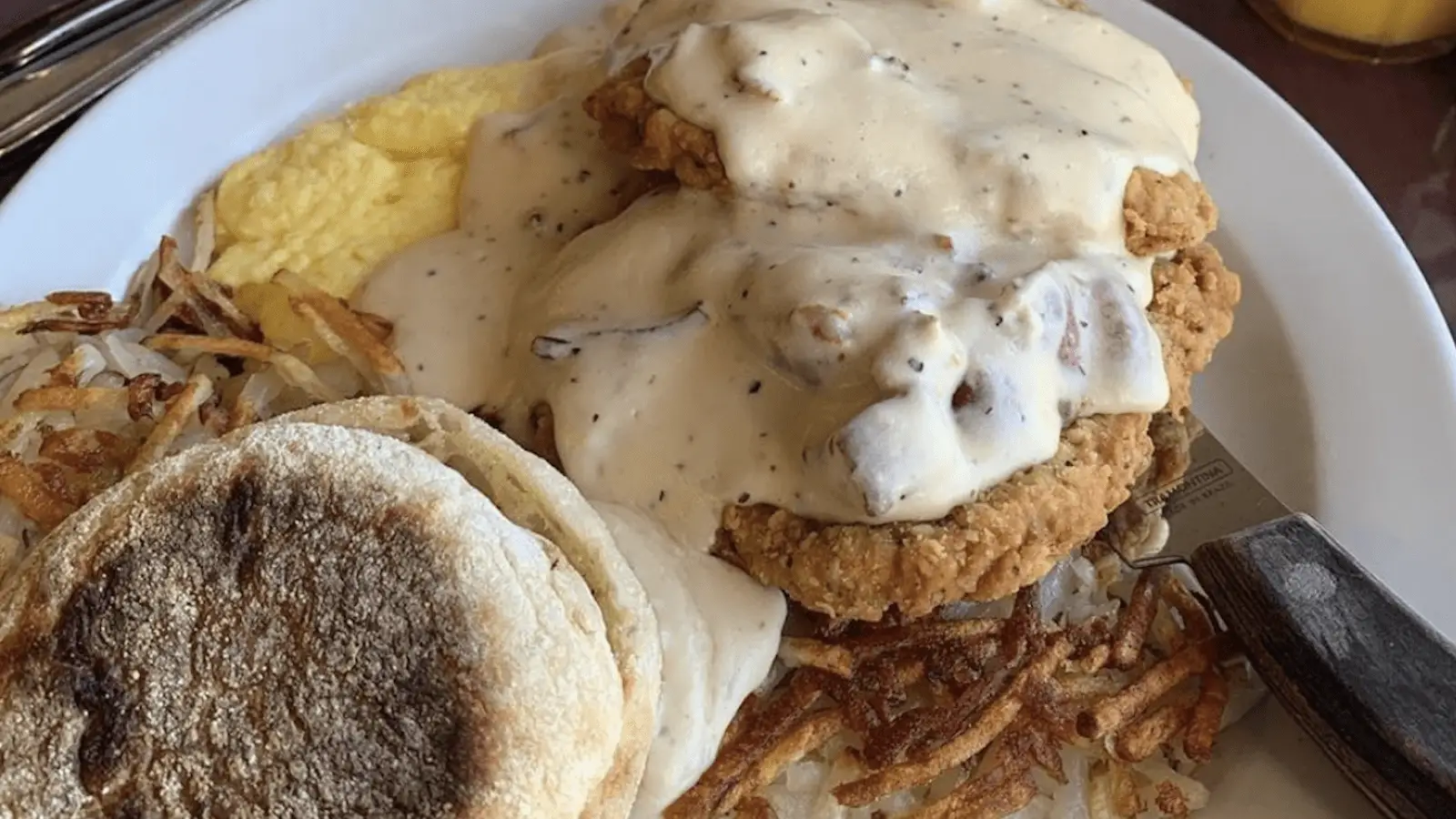 A plate of the Best Breakfast in North Bay features chicken fried steak with creamy gravy, scrambled eggs, a toasted English muffin, and crispy hash browns.