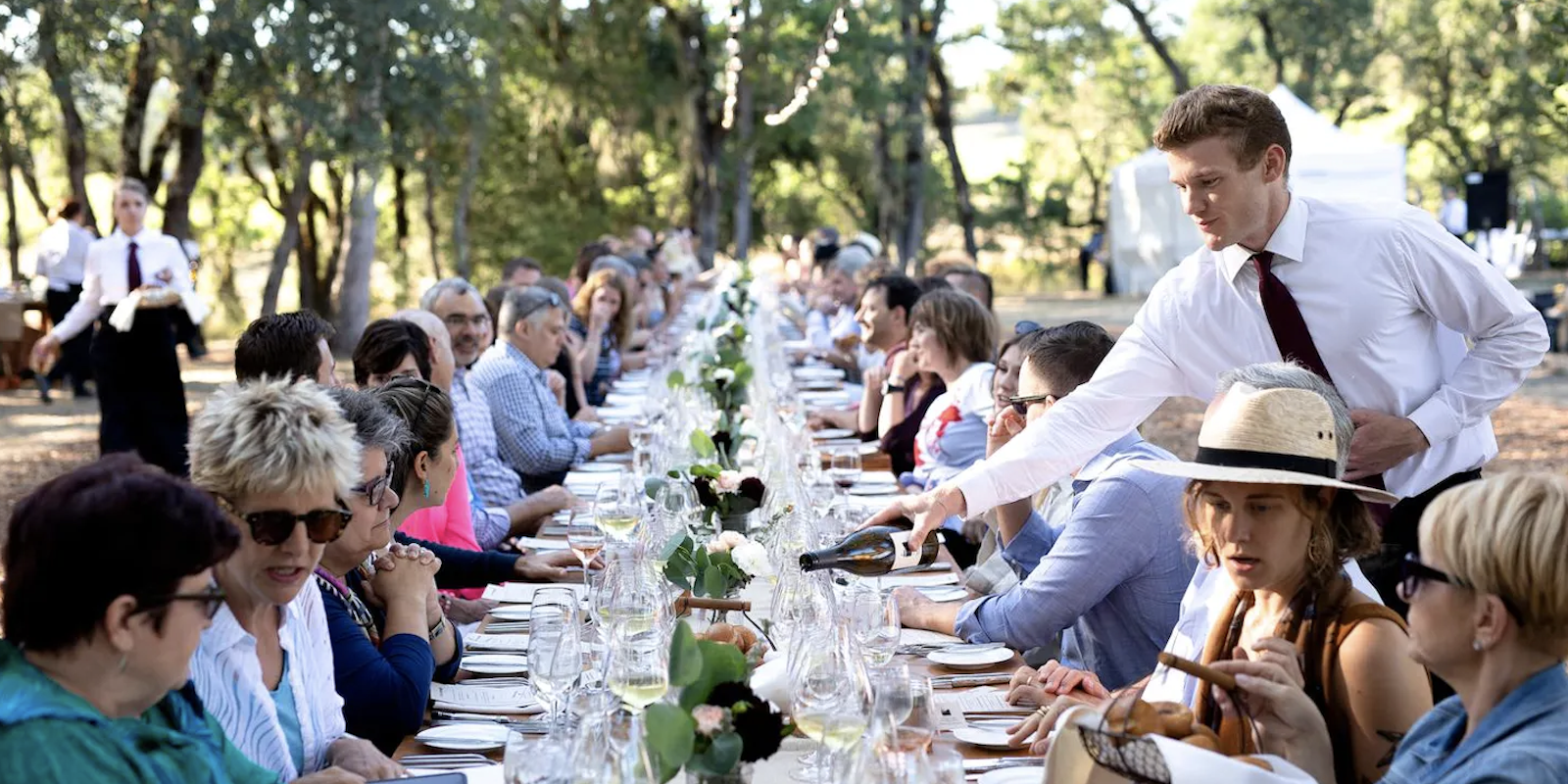 Waiter pours wine at long dinner table for Medlock Ames' Dinner in the Vineyard, Sonoma, California