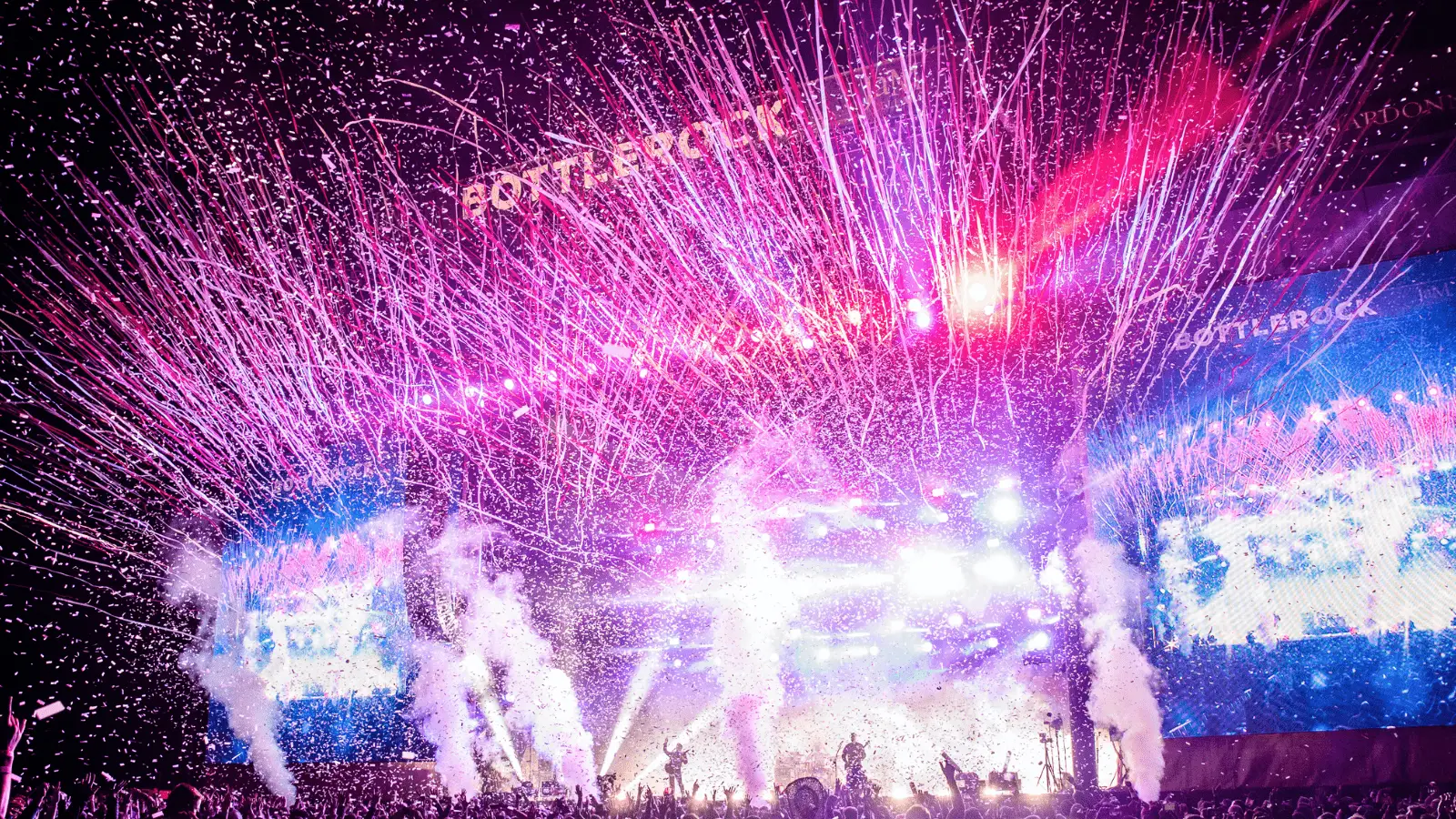 A vibrant concert stage with bright fireworks and confetti fills the scene. Colorful lights illuminate the area, creating a dynamic and festive atmosphere. The BottleRock festival banner is visible amidst the spectacle, showcasing one of the Best Annual Events in the North Bay, with a lively crowd enjoying the performance.