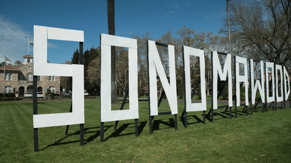 A large sign with tall, white letters spells out "SONOMAWOOD" in a park-like setting. The letters are mounted on black frames. In the background, there are trees, a historic building with a clock tower, and a clear blue sky—one of the best things to do in Sonoma this March.