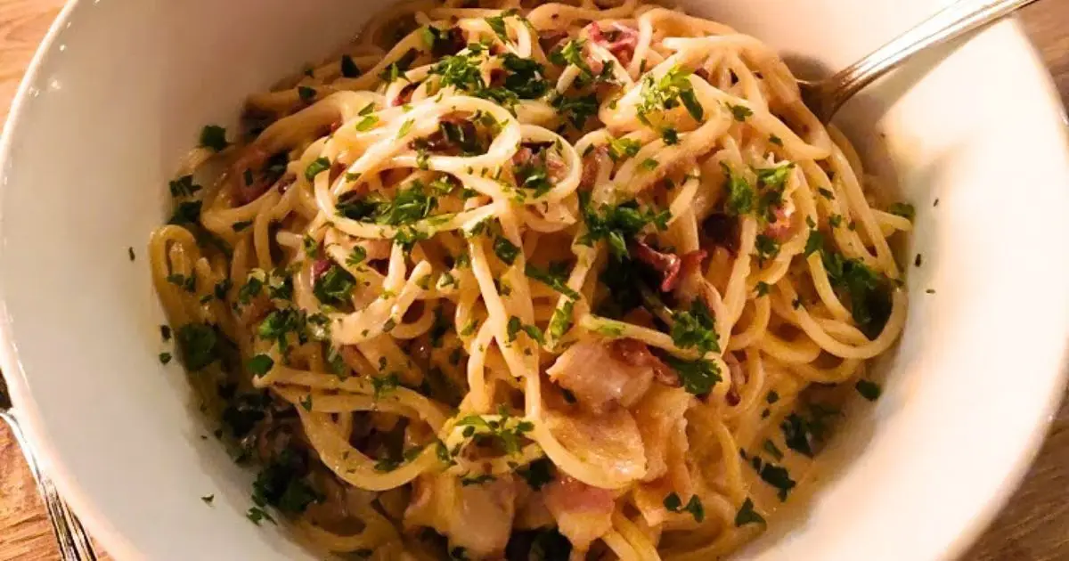 A bowl of spaghetti carbonara with a creamy sauce, garnished with chopped parsley. The dish includes pieces of pancetta or bacon, and a fork is resting on the side of the bowl. For the best dinner San Francisco has to offer, this appetizingly arranged pasta is a must-try, ready to be eaten.